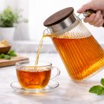 glass water pitcher with wooden handle, stainless steel filter lid and anti-drip spout for hot and cold beverages – available at Homedash Lebanon.