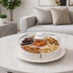 Round divided snack tray with clear cover and 6 compartments filled with nuts and dried fruits on a modern table