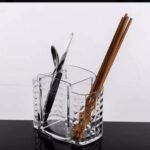 Transparent acrylic storage organizer with multiple compartments for kitchen utensils and makeup brushes on a white background
