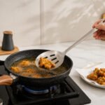 Long stainless steel slotted spoon with ergonomic handle used for frying and serving food in kitchen.