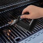 Black 3-in-1 grill cleaning brush with stainless steel bristles, metal scraper, scouring pad, and ergonomic long handle for BBQ cleaning.