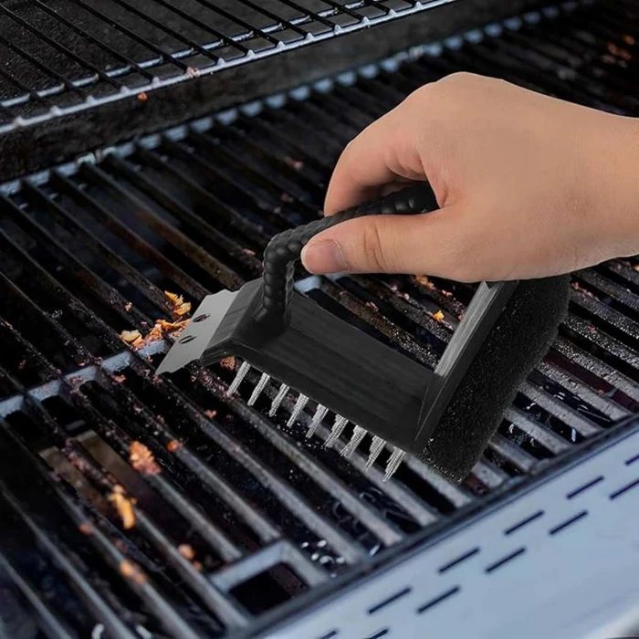Black 3-in-1 grill cleaning brush with stainless steel bristles, metal scraper, scouring pad, and ergonomic long handle for BBQ cleaning.
